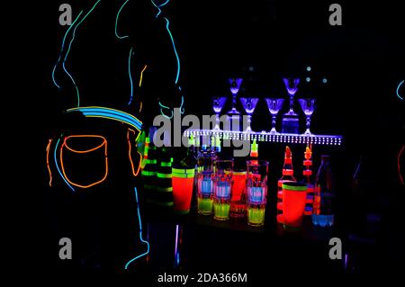 Barman professionista e spettacolo di luci a LED. Silhouette di moderno barman scuotendo drink al cocktail bar serale. Foto Stock