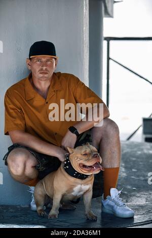 giovane uomo vestito con stile con il cane bully americano in città strade Foto Stock
