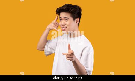 Uomo che punta il dito indice sulla fotocamera, facendo gesti del telefono Foto Stock