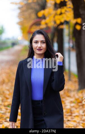 Ritratto di una giovane donna in autunno. Scenario con luce calda e foglie cadenti. Guarda alla fotocamera. Foto Stock