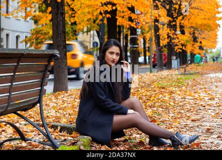 Ritratto di una giovane donna in autunno. Scenario con luce calda e foglie cadenti. Foto Stock