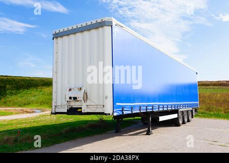 Un nuovissimo rimorchio blu per veicoli industriali in attesa sulla strada in un campo, in una giornata estiva brillante Foto Stock