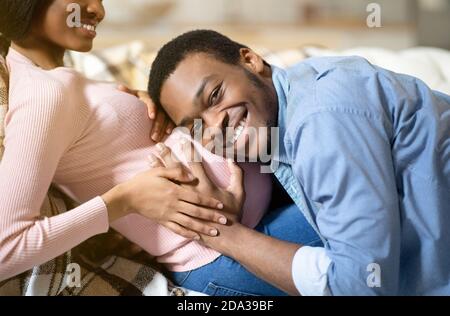 Felice uomo nero abbracciando la sua ragazza incinta grande ventre e. ascoltare il battito cardiaco del bambino non ancora nato a casa Foto Stock
