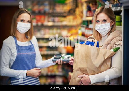 Donna adulta in maschera medica che raccoglie ordine in drogheria negozio Foto Stock