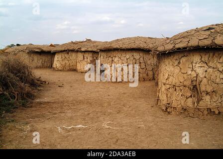 Vista del villaggio di Masai con vecchie capanne di argilla e solo piccolo ragazzo vicino muro di argilla. Povertà, miseria, vivere in Africa. Kenya. Masai Mara Foto Stock