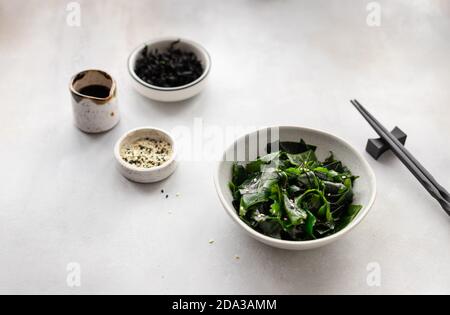 wakame alghe in un recipiente con salsa di soia e semi di sesamo su sfondo grigio. Foto Stock