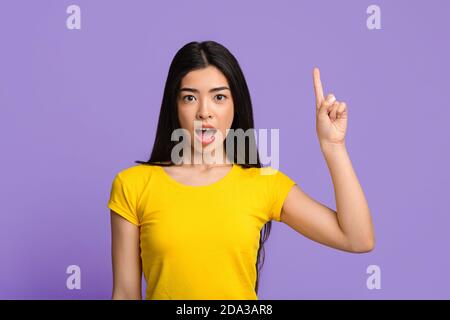 Ottima idea. Eccitato giovane donna asiatica che punta il dito in su avendo momento di ispirazione Foto Stock