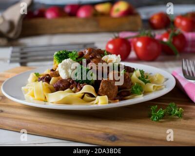 delizioso gulasch di fagioli di maiale con crema acida e pasta su una piastra Foto Stock