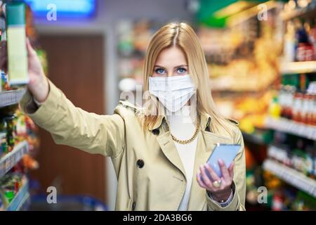 Donna adulta in maschera medica utilizzando smartphone e lo shopping per generi alimentari Foto Stock