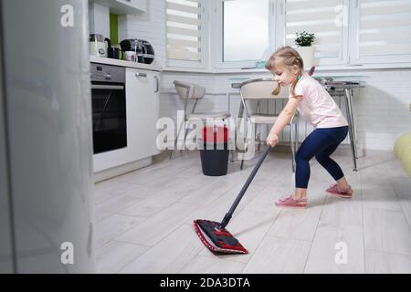 bambina lava il pavimento in cucina con un mop Foto Stock