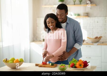 Bella coppia incinta nera che fa insalata di verdure in cucina, copia spazio Foto Stock