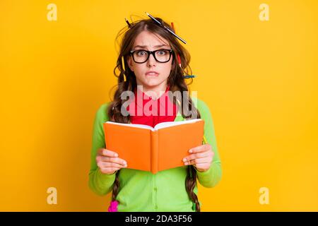 Primo piano ritratto di attraente funky preoccupato adolescente ragazza di lettura esercizio libro mordere labbro isolato su sfondo di colore giallo brillante Foto Stock