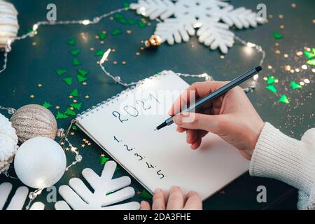 Gli obiettivi di Capodanno. Anno 2021. Mano della donna che scrive la lista in un blocco note. Concetto di motivazione delle aspirazioni di risoluzione Foto Stock