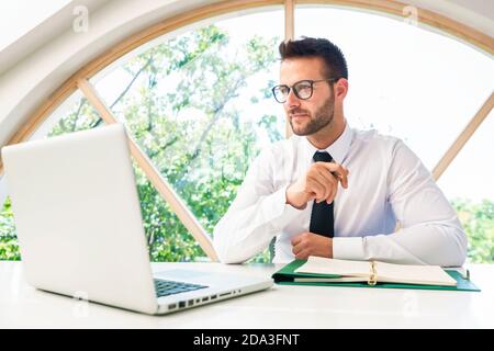 Bell'uomo d'affari che guarda con attenzione mentre si lavora alla scrivania dell'ufficio in ufficio. Foto Stock
