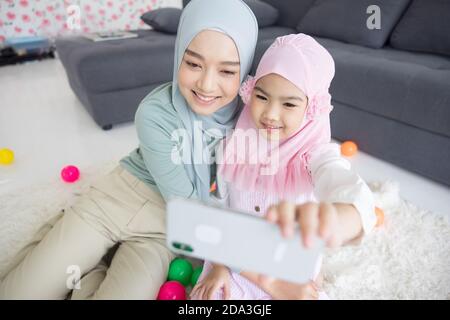 madre musulmana futura maternità in hijab e prendendo auto ritratto in soggiorno Foto Stock