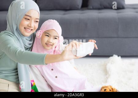 madre musulmana futura maternità in hijab e prendendo auto ritratto in soggiorno Foto Stock