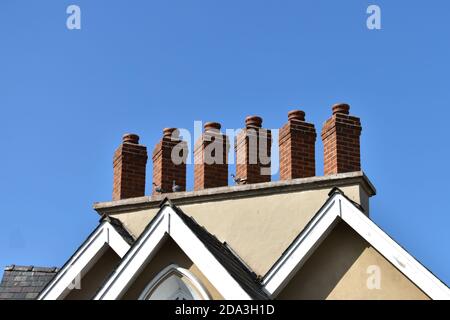 primo piano di 6 insoliti e attraenti camini costruiti in mattoni seduti sul tetto della casa che mostra gli apici con fondo blu profondo del cielo Foto Stock