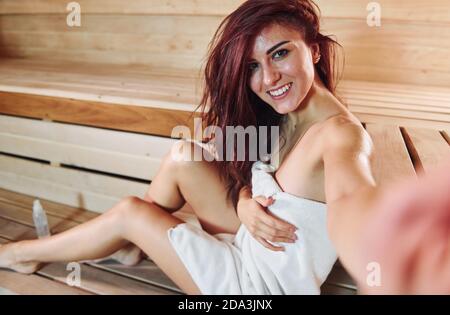 Giovane bella donna si riposa nella sauna. Fare selfie Foto Stock