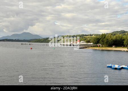 Loch lomond in una giornata estiva nuvolosa con un grande traghetto barche per escursionisti e pedalò Foto Stock