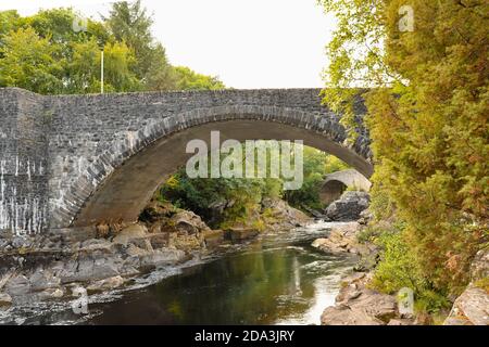 primo piano di vecchio ponte di pietra che attraversa un fiume in highlands scozia circondata da lussureggianti alberi verdi in estate Foto Stock