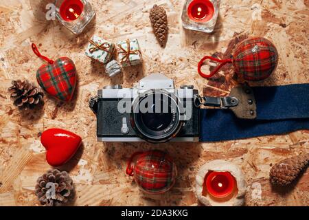 La natura morta del Natale con una classica macchina fotografica d'epoca, decorazioni sugli alberi, candele rosse, piccoli gif e pinecones su un tavolo di legno Foto Stock