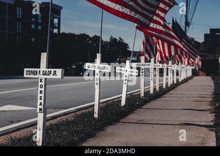 DULUTH, STATI UNITI - 07 novembre 2020: Duluth, Georgia / Stati Uniti - 6 novembre 2020: Croci bianche e bandiere americane fiancheggiano una strada cittadina in memor Foto Stock