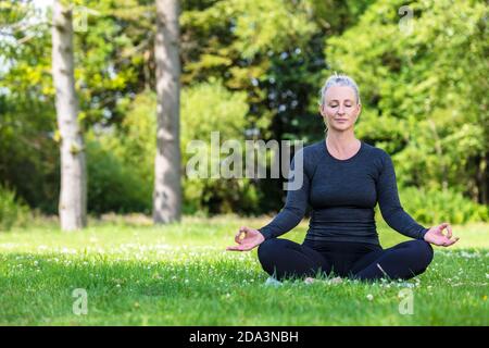 Mature metà età misura donna sana praticando yoga outsiin A. ambiente naturale tranquillo e verde Foto Stock