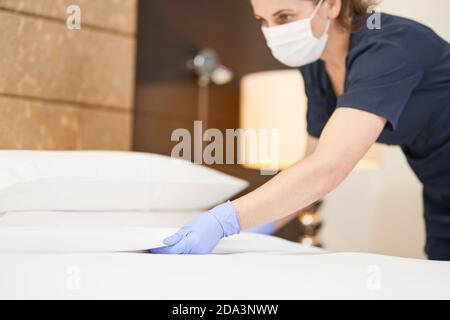 Cameriera in maschera che copre la coperta sul letto in Il concetto di servizio in camera dell'hotel Foto Stock