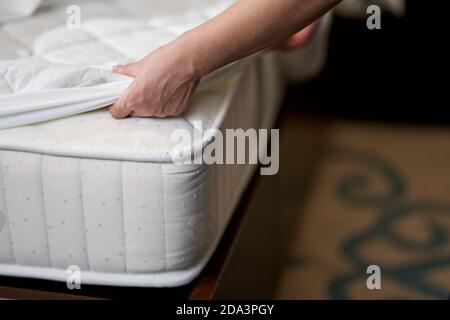 Primo piano di pulizia della cameriera che cambia foglio pulito sul materasso bianco in camera d'albergo durante la pulizia. Concetto di servizio alberghiero Foto Stock