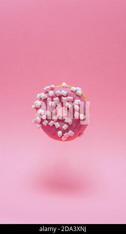 Primo piano di una ciambelle che si levitano su sfondo rosa. Fotografia verticale Foto Stock