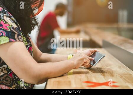 Donna che usa telefoni cellulari per lavorare con immagine sfocata di il contrassegno di posto alternativo per la distanza sociale regola la distanza per uno sedile da altre persone a. Foto Stock