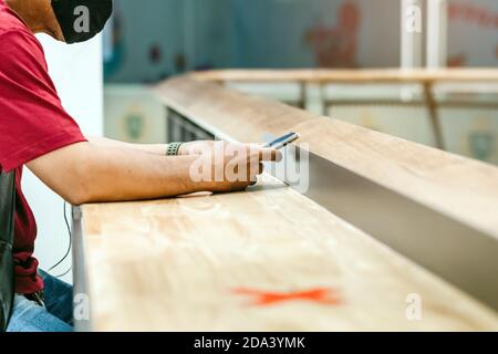 Uomo che usa telefoni cellulari per lavorare con immagine sfocata di il contrassegno di posto alternativo per la distanza sociale regola la distanza per uno posto da altre persone a p. Foto Stock