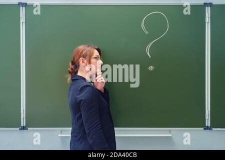 L'insegnante è pensieroso di fronte a un punto interrogativo scritto su una lavagna. Problemi di educazione e difficoltà nell'insegnamento di st Foto Stock