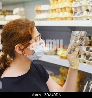 Donna adulta in maschera medica compra uova di quaglia in un supermercato Foto Stock