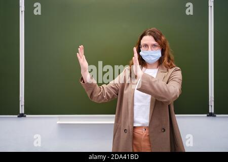 Insegnante nella maschera medica mostra il gesto - mantenere la distanza, spazio di copia. Concetto di formazione per la quarantena scolastica Foto Stock