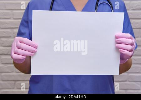 Una dottoressa contiene un foglio vuoto, spazio di copia per il testo. Mani di un infermiere in guanti medici protettivi con un foglio bianco, primo piano Foto Stock