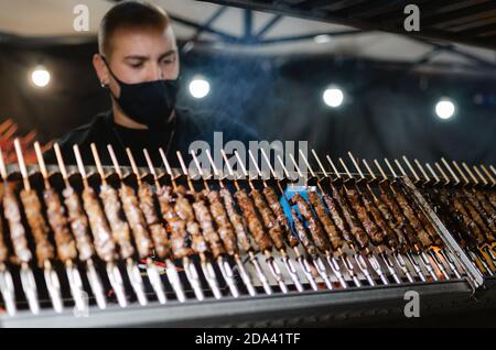 Cuneo, Italia - 3 ottobre 2020: Arrosticini tradizionali abruzzesi (spiedini tipicali) cucinati di notte da un giovane che indossa una maschera protettiva su una stre Foto Stock