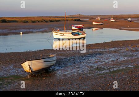 Piccole barche in acque basse a Overy Creek in bassa luce serale nel Nord Norfolk a Burnham Overy Staithe, Norfolk, Inghilterra, Regno Unito. Foto Stock