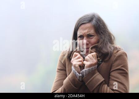 Stressata donna di mezza età che ottiene freddo giacca grabbing lamentando dentro inverno in piedi all'aperto Foto Stock