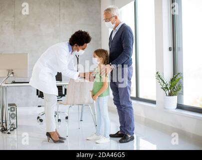 Uomo anziano con la sua piccola grandaughter all'esame del pediatra Da una dottoressa afroamericana Foto Stock