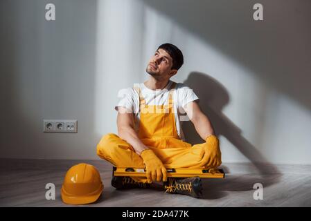 Un uomo di mano stanco in uniforme gialla si siede all'interno e si rompe. Ristrutturazione casa concezione Foto Stock