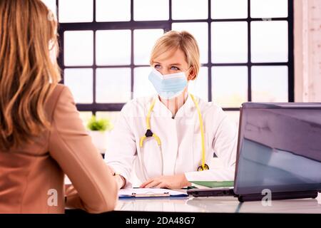 Foto di una bella dottoressa che parla con il paziente mentre si siede alla scrivania in camera del medico. Foto Stock