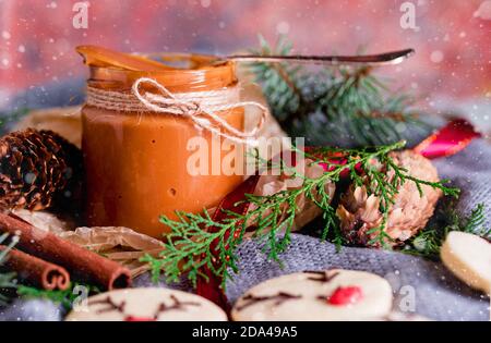 Un piccolo vasetto con latte condensato fatto in casa bollito. Shortbread biscotti di Natale, luci, sprigs di abete rosso, urti. Contenuti di Capodanno. Foto Stock