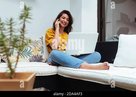 Donna che parla al telefono mentre lavora con il suo laptop da casa. Foto Stock