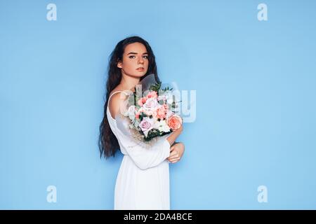 Giovane donna in abito bianco con un bel bouquet di rose, su sfondo blu. Foto Stock