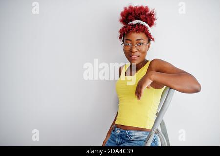 Donna afroamericana in singlet giallo e occhiali da vista contro parete bianca stand om scala in ferro. Foto Stock