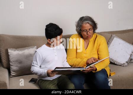 Momenti felici con la nonna, signora superiore indiana/asiatica che passa il tempo di qualità con il suo libro di lettura del figlio grande insieme. Foto Stock