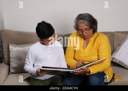 Momenti felici con la nonna, signora superiore indiana/asiatica che passa il tempo di qualità con il suo libro di lettura del figlio grande insieme. Foto Stock