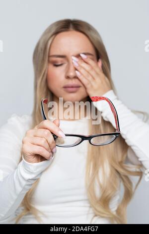 Donna con occhiali che tengono in mano sfregando gli occhi, si sente stanca dopo aver lavorato sul laptop, messa a fuoco morbida. Concetto di overwork. Sfinito e faticoso ragazza Foto Stock