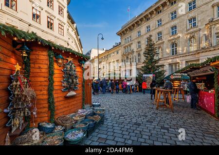 Persone che camminano tra chioschi di legno e bancarelle in strada acciottolata a Vienna, Austria. Foto Stock